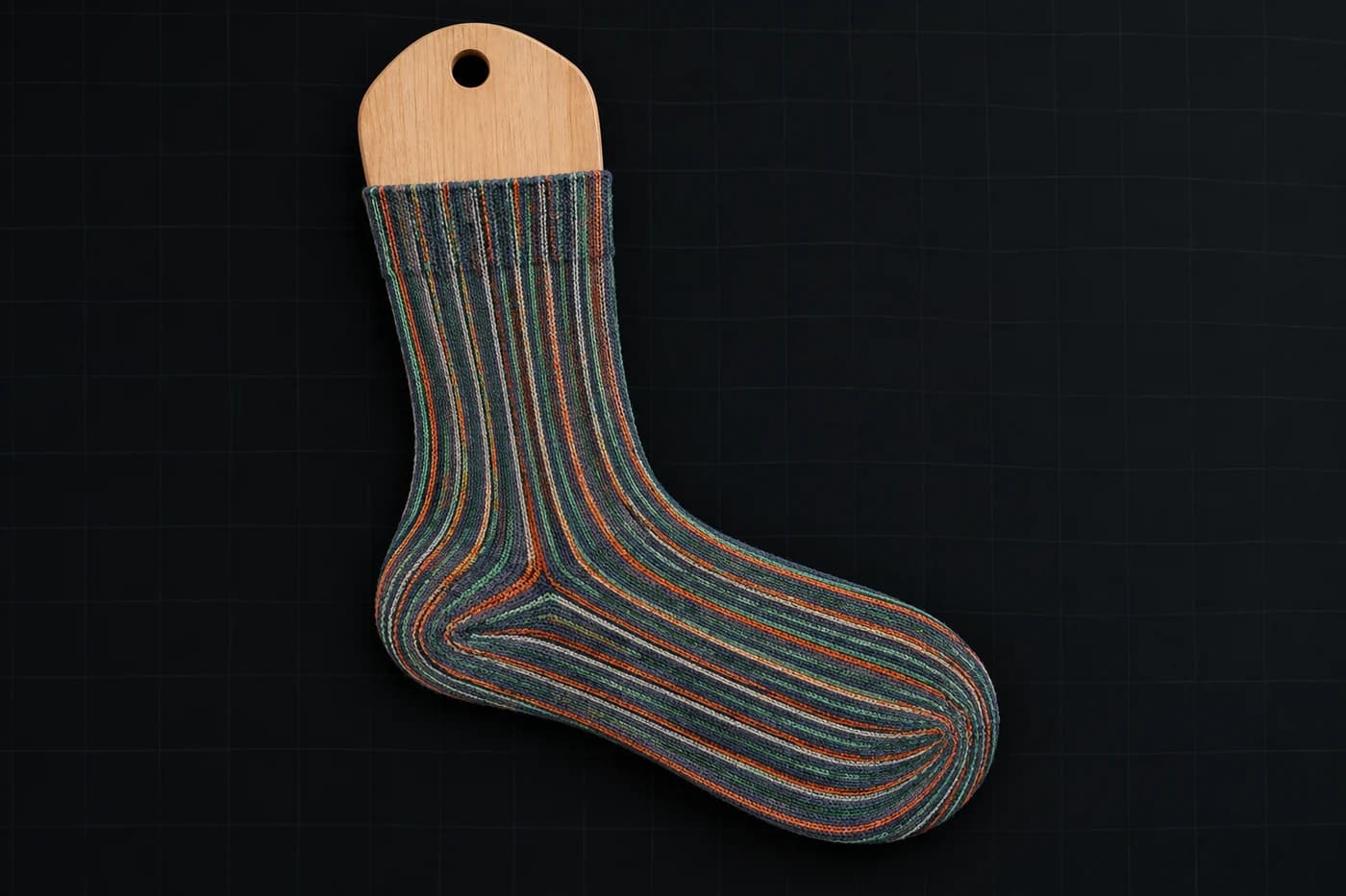 Fine pinstripe on a sock form. Lengthwise lines spread widest exactly where they are most visible. Modelled stretch, not a photograph of a worn sock.